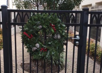 A christmas wreath is hanging on a fence behind a gate.