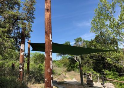 A green tarp is hanging from a wooden pole in the middle of a forest.
