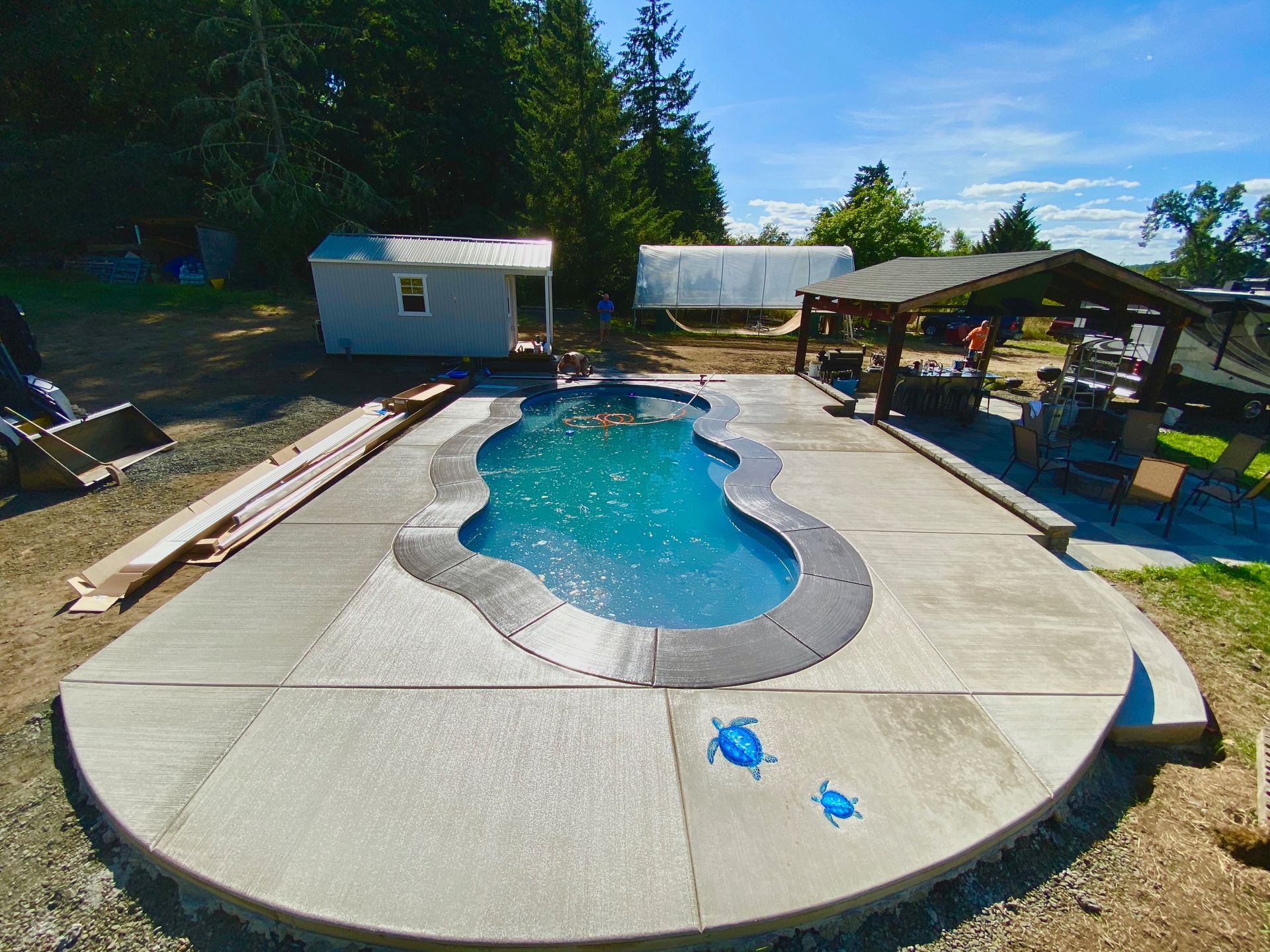 Backyard swimming pool with concrete deck, lounge area, and trees in the background
