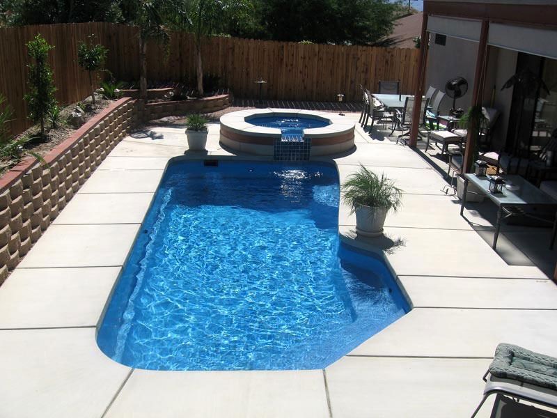 Backyard with a narrow blue pool and raised spa, surrounded by stone patio and lounge chairs