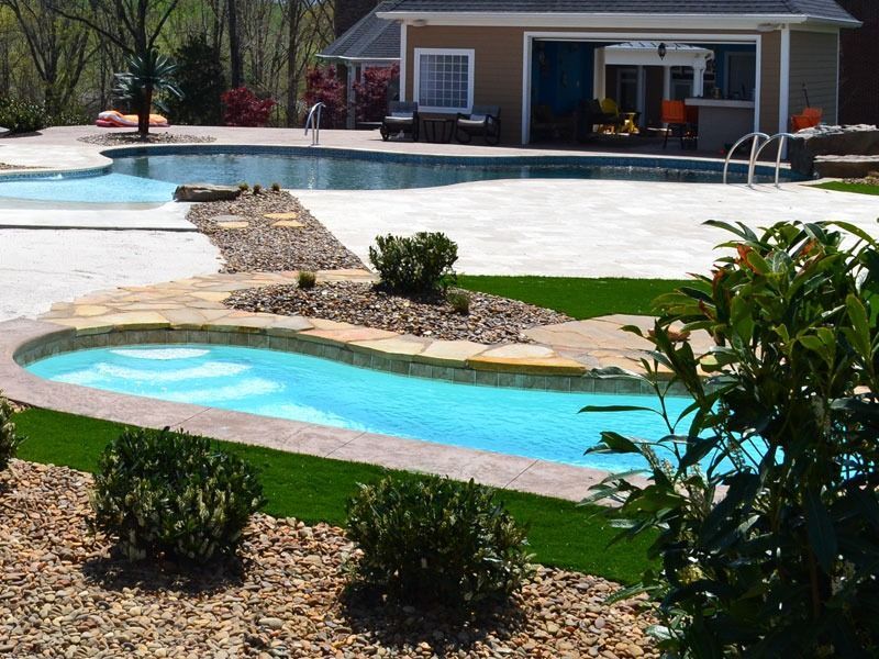 Backyard with curving turquoise pool, stone path, green lawn, and a small pool house in the background
