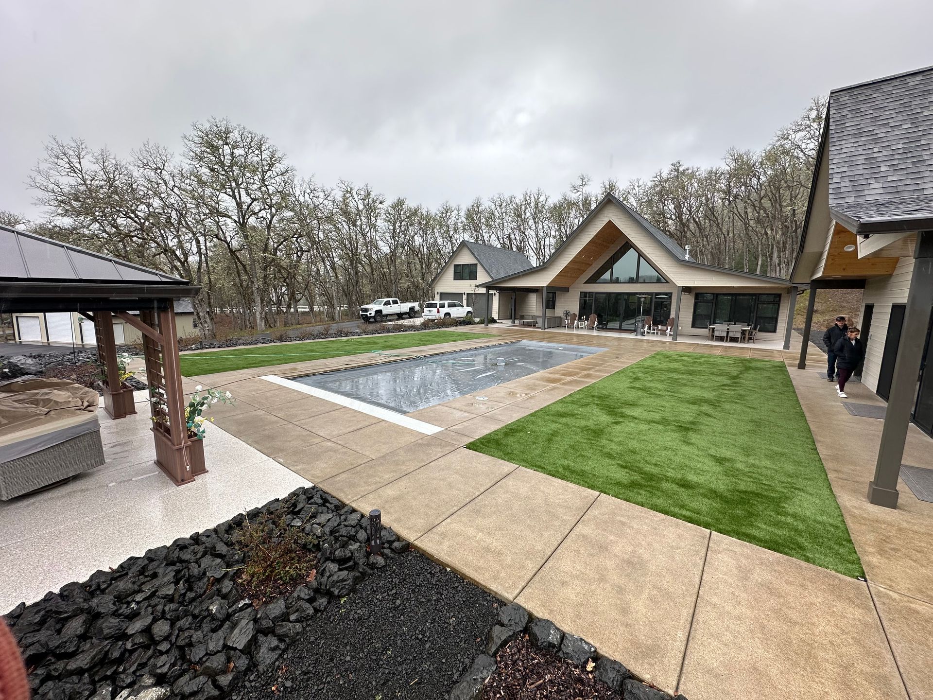 Modern house courtyard with long reflecting pool, green lawn, stone paths, and cloudy sky