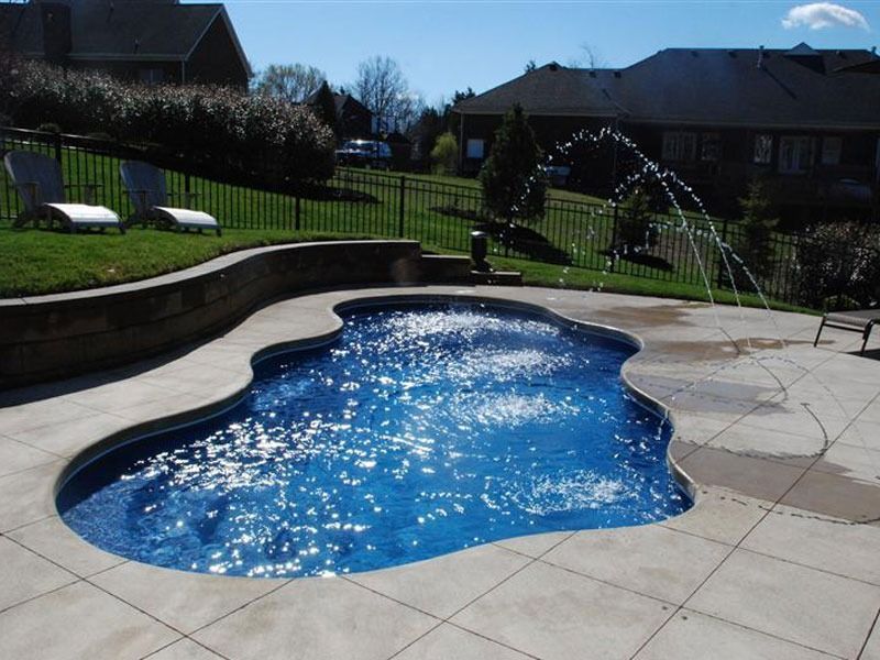 Backyard pool with blue water, curved stone edge, and lawn in the background