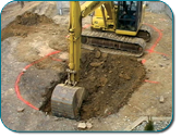 Excavator digging soil in a dirt excavation site, with a marked circular area around the work zone.