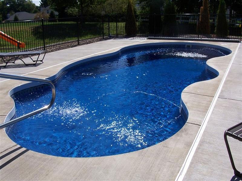 Freeform blue backyard swimming pool with a curved edge and diving board, surrounded by a concrete deck.