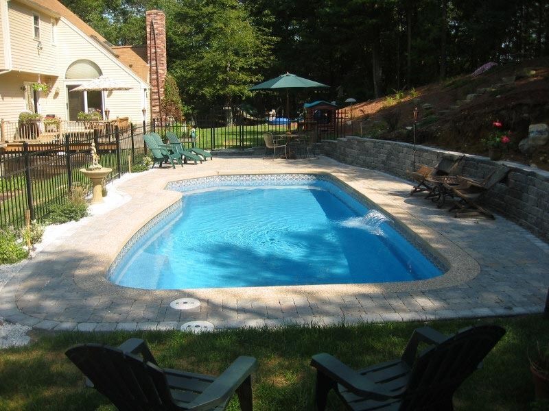 Backyard swimming pool with patio chairs, stone deck, and shaded seating area