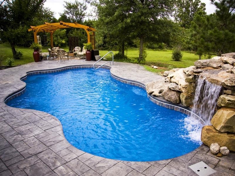 Backyard swimming pool with a stone waterfall, patio, and a wooden pergola seating area