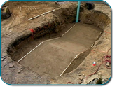 Archaeological excavation pit with exposed soil walls and a marked rectangular burial outline