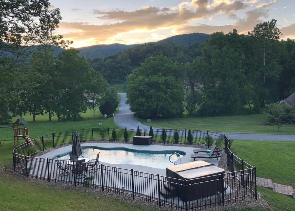 Fenced outdoor pool overlooking green hills at sunset, with lounge chairs and a cloudy sky.