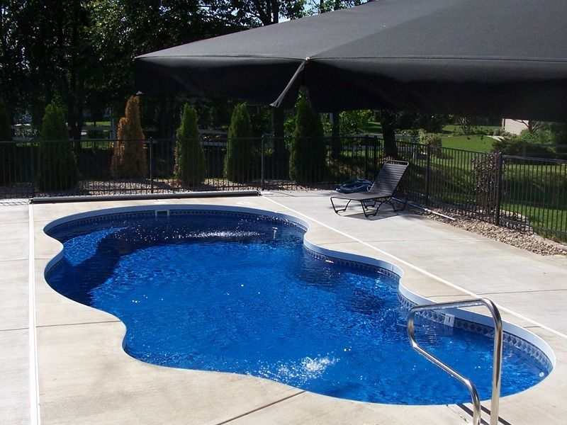 Backyard swimming pool with blue water, surrounded by patio, fence, and shade canopy