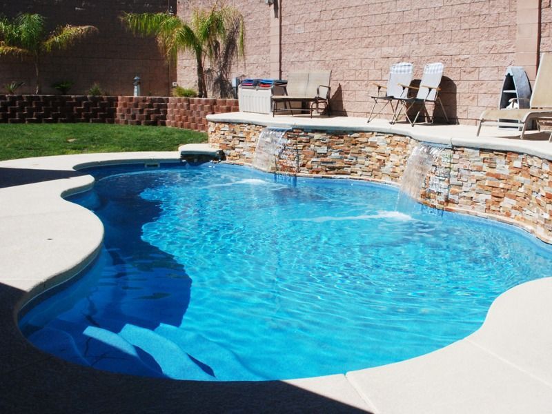 Backyard swimming pool with blue water, stone coping, and lounge chairs on a sunny patio