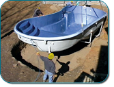 Worker lifting a blue-and-white fiberglass boat shell at a construction site