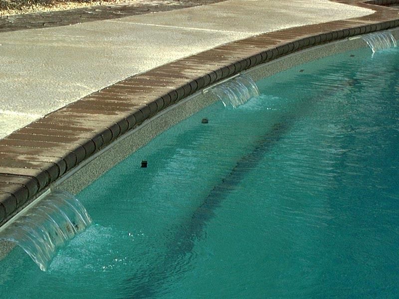 Curved swimming pool edge with turquoise water and a beige deck beside it