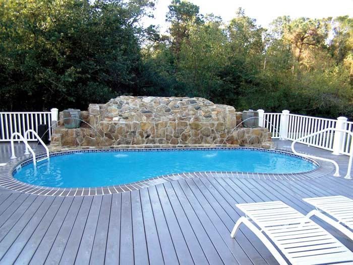 Backyard pool with blue water, white deck chairs, and a stone waterfall backdrop