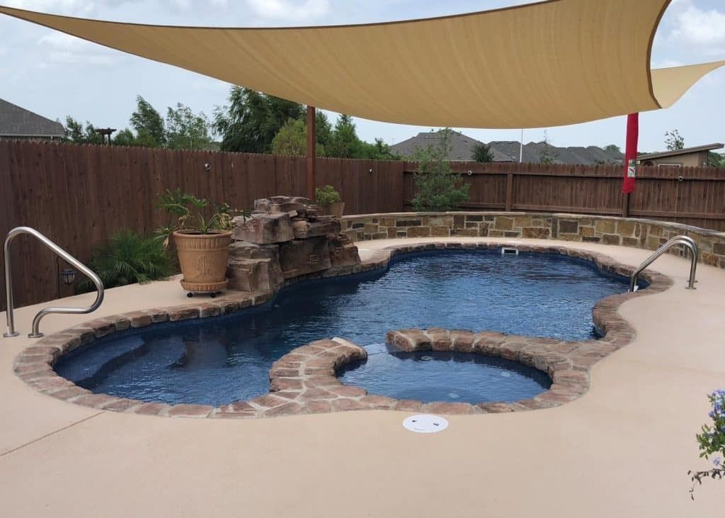 Backyard pool with tan shade sail, stone waterfall, and curved spa area
