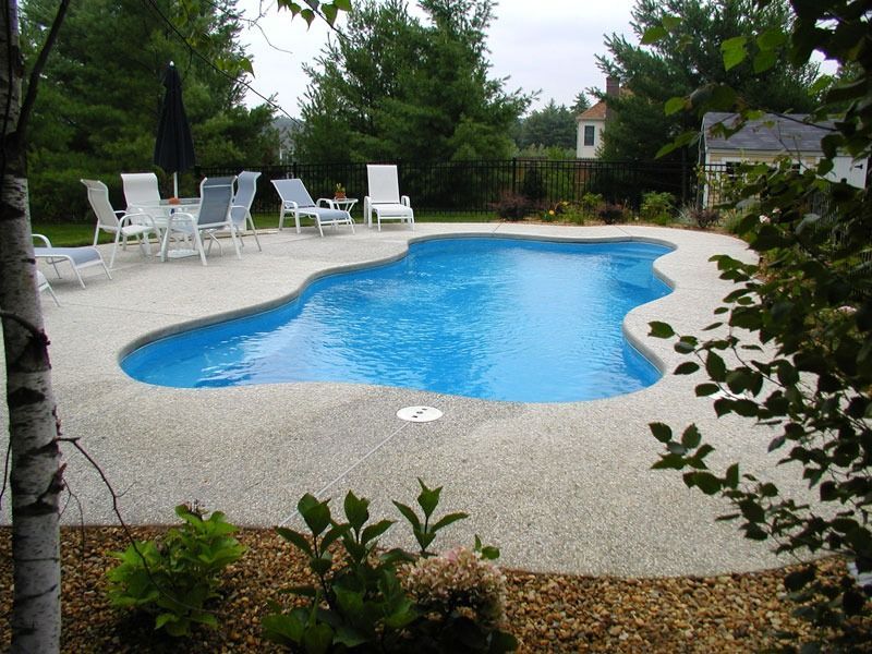 Backyard swimming pool with white lounge chairs and umbrellas, surrounded by greenery