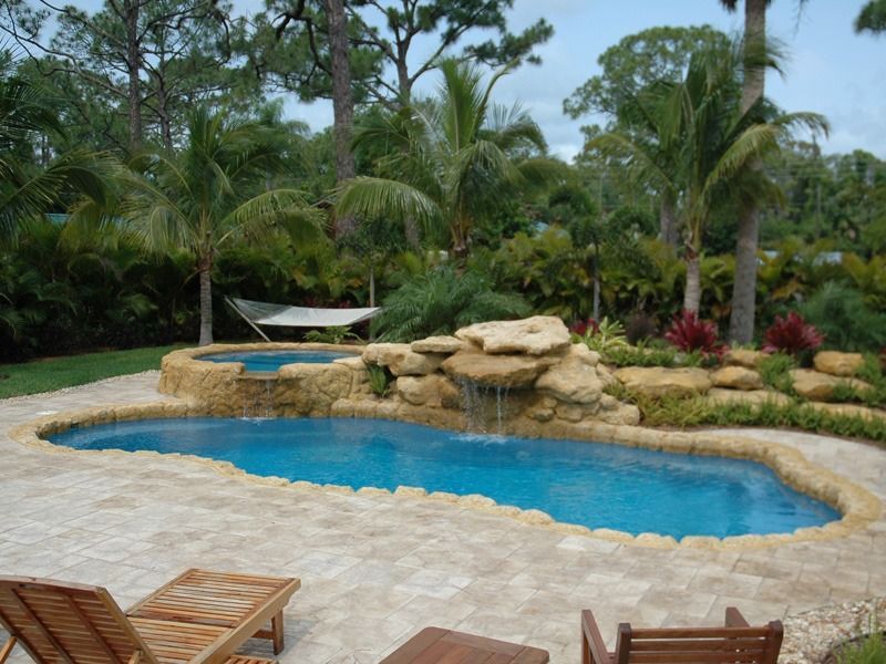 Backyard pool with rock waterfall, palm trees, and a hammock in a tropical landscaped garden