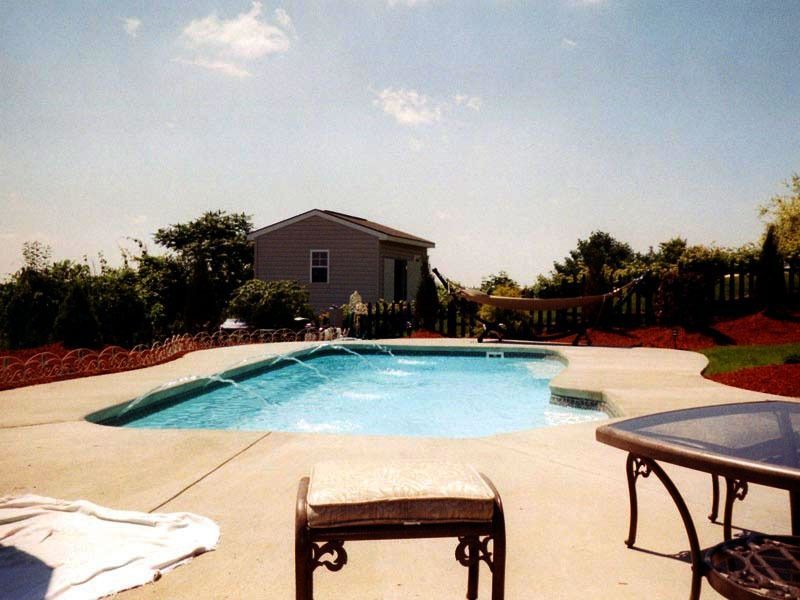 Backyard swimming pool with lounge chairs, table, and a small house in the background