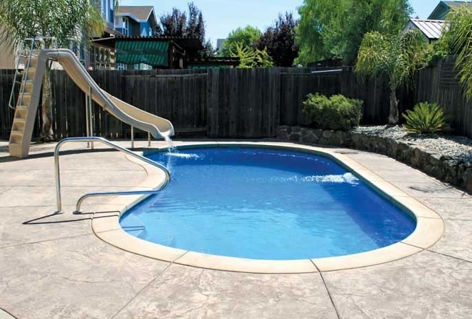 Backyard swimming pool with a slide, ladder, and concrete deck surrounded by a fence and trees