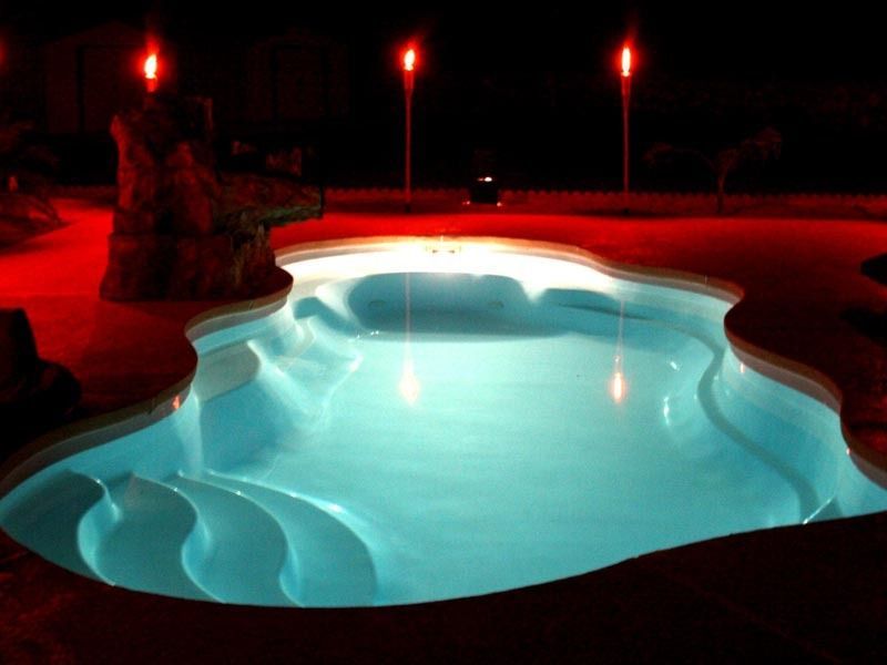 Red-lit outdoor swimming pool at night with glowing blue water and surrounding deck lights