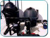 Two black dome-shaped industrial machines with pipes and legs on a white floor against a plain background