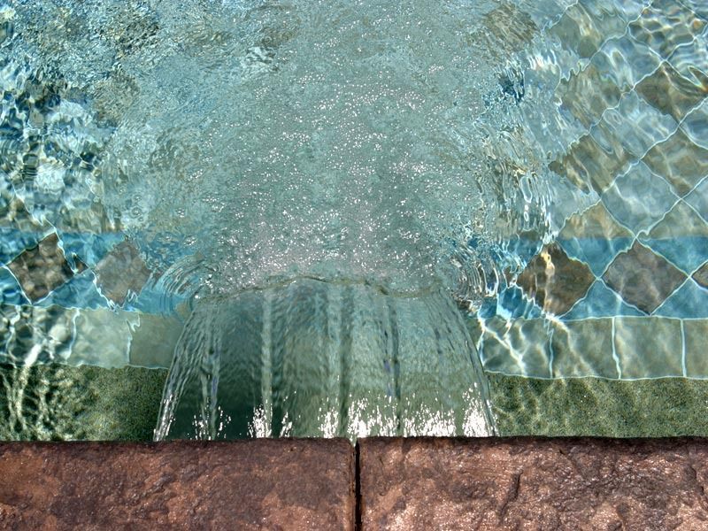 Water bubbling up through a tiled fountain over a stone border.
