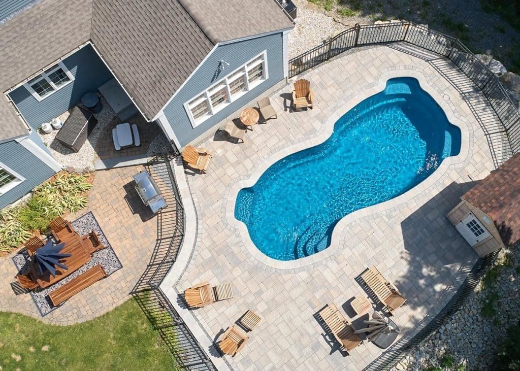 Aerial view of a backyard patio with a blue swimming pool, lounge chairs, and a house.