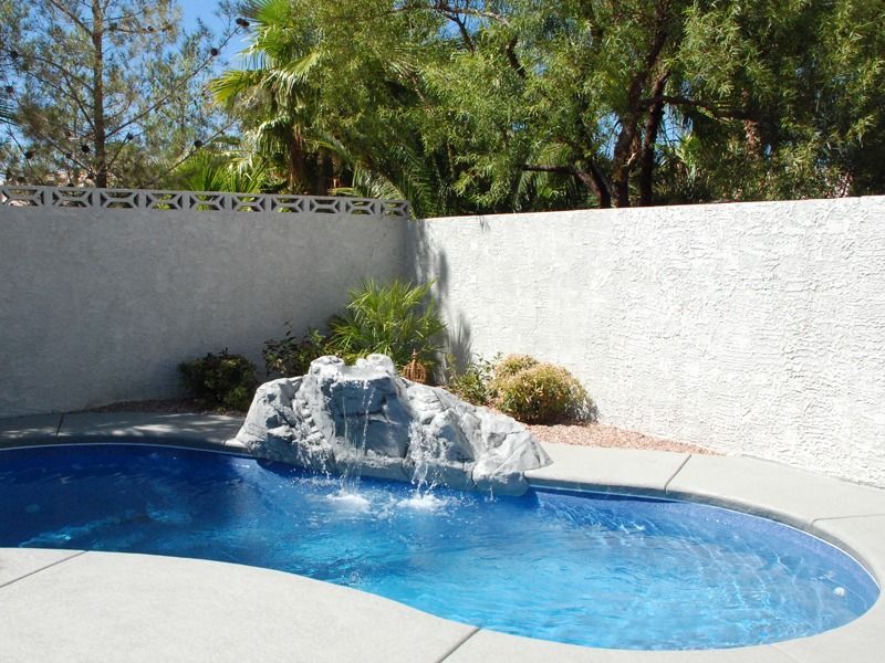 Backyard swimming pool with a rock waterfall and white stucco walls under trees