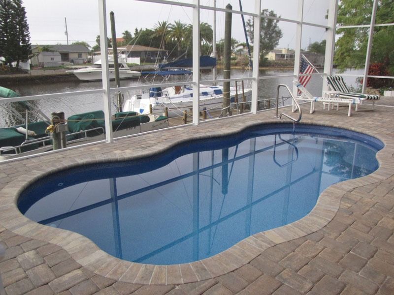 Small backyard pool with blue water beside a canal and patio chairs behind a fence