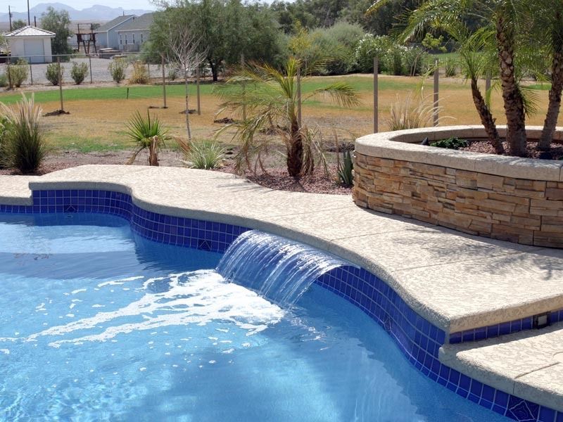 Backyard swimming pool with a small waterfall, blue tile, stone coping, and landscaped patio.