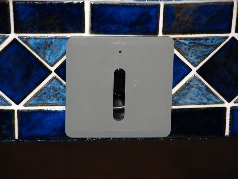 Gray dispenser mounted on a blue-and-black tiled wall
