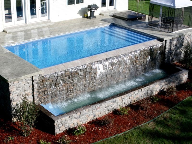 Backyard pool with a stone water feature spilling into a lower basin and landscaped mulch border