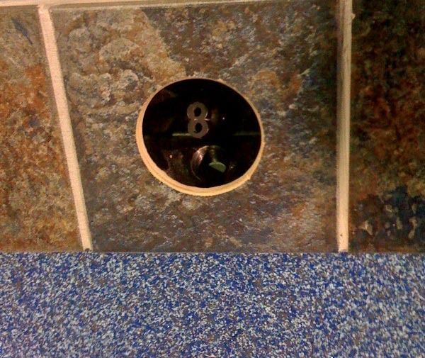 Close-up of a tiled wall with a round black 8-ball-style sign above blue carpet.