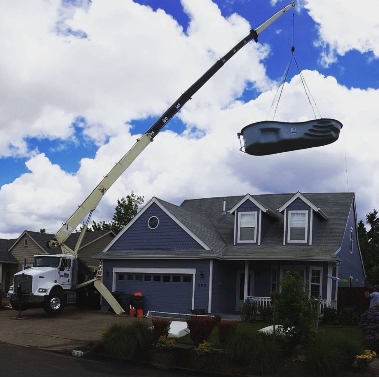 A moving truck hoists a couch above a blue house under a partly cloudy sky.
