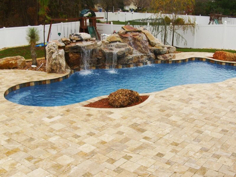 Backyard pool with rock waterfall, blue water, and tan stone patio