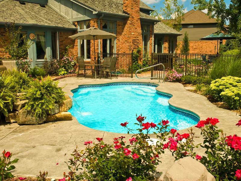 Backyard pool with stone patio, lounge chairs, and bright flowers in front of a house