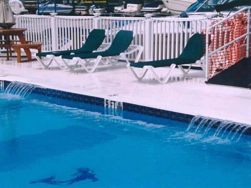Outdoor pool with blue water, white lounge chairs, and green towels near a deck fence