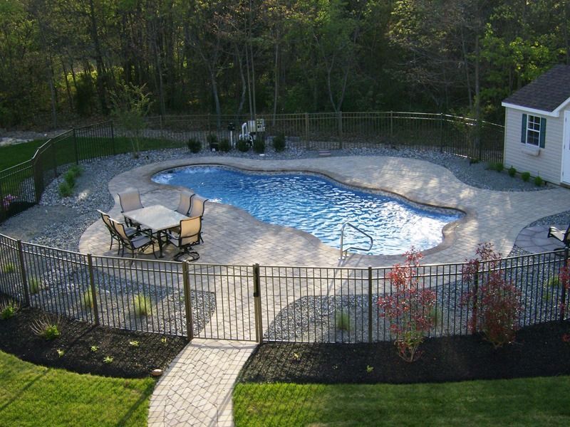 Backyard swimming pool with stone deck, patio table, and black metal fence, seen from above