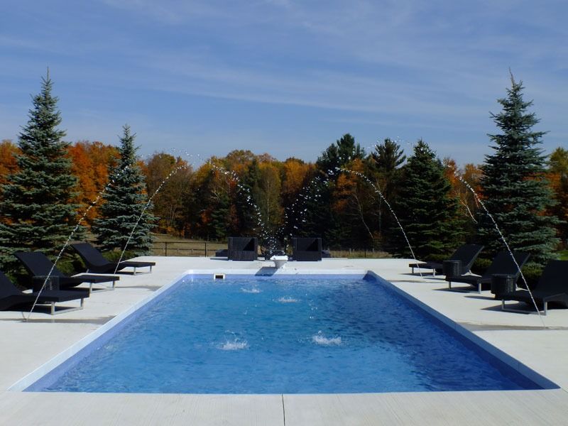 Outdoor pool with blue water, black loungers, and autumn trees under a clear sky