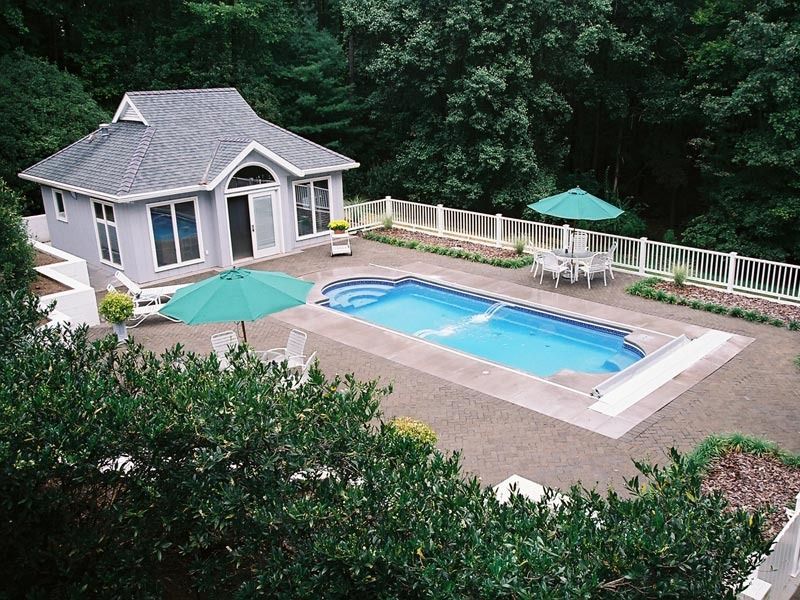 Backyard with a swimming pool, small pool house, and green patio umbrella surrounded by trees