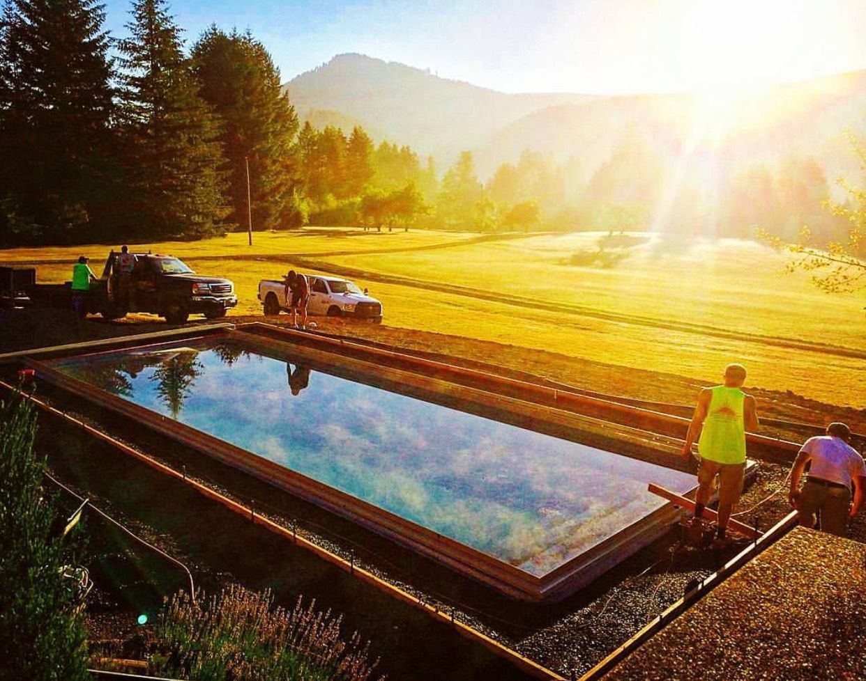 Sunlit outdoor pool reflecting mountains, with people working beside it on a rural farm