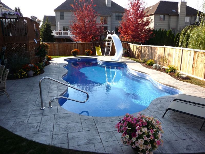 Backyard pool with a blue slide, patio chairs, and flowering plants in bright sunlight