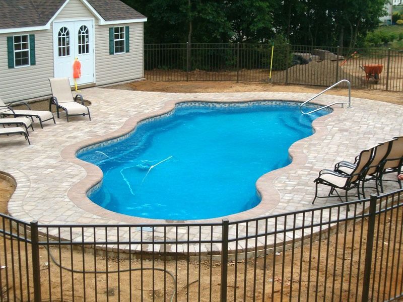Backyard swimming pool with blue water, stone patio, lounge chairs, and a small pool house