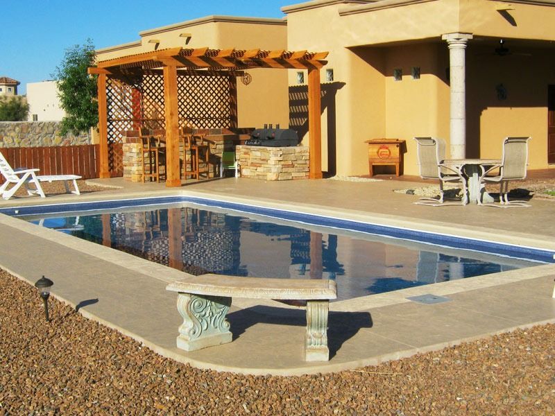 Backyard swimming pool with lounge chairs and a pergola beside a beige house under bright sunlight