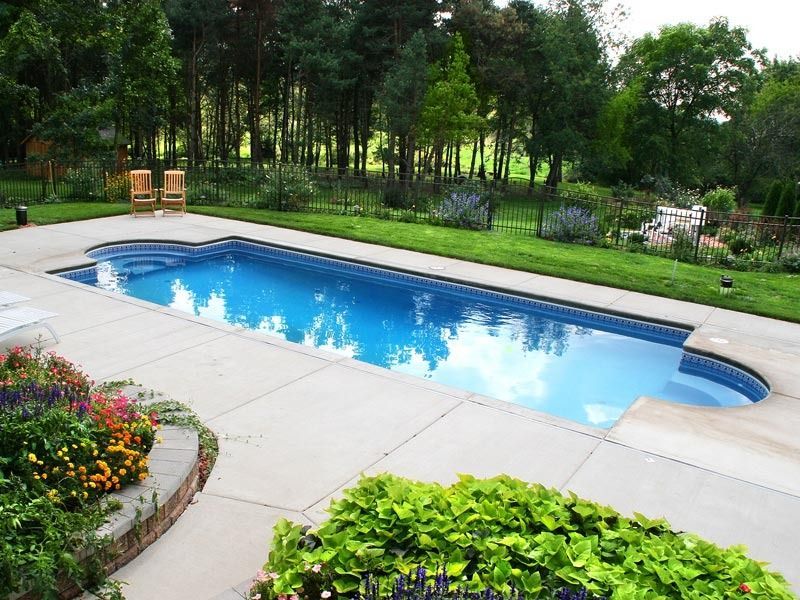 Backyard swimming pool with blue water, stone patio, flowers, and lush green trees