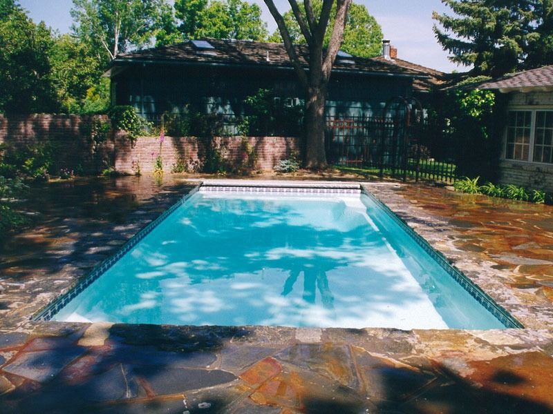 Backyard swimming pool with turquoise water, brick deck, and trees casting shade around it