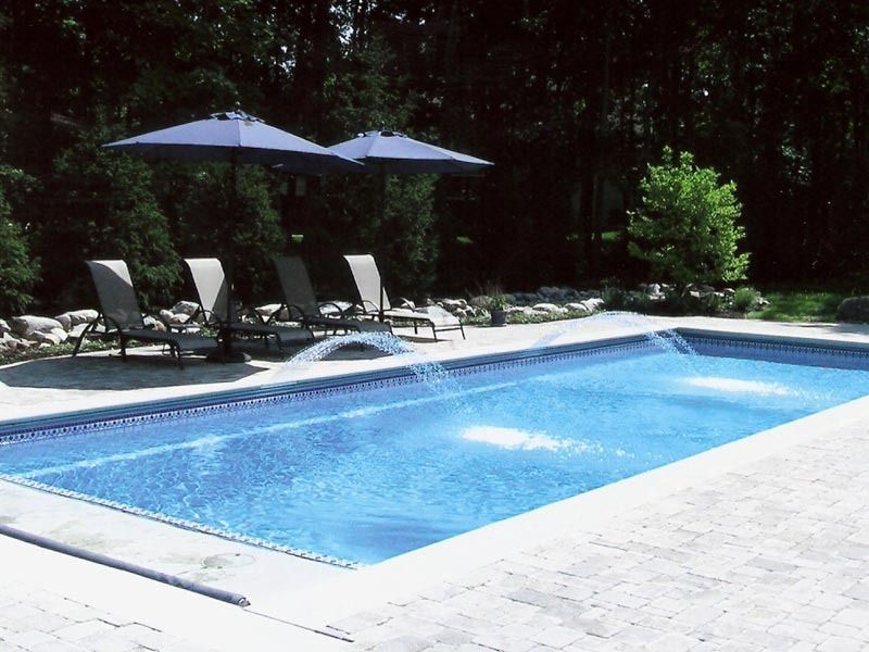 Backyard swimming pool with lounge chairs, blue umbrellas, and surrounding trees