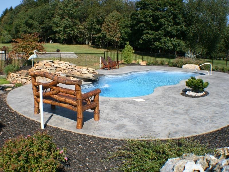Backyard pool with stone deck, wooden bench, and trees in the background