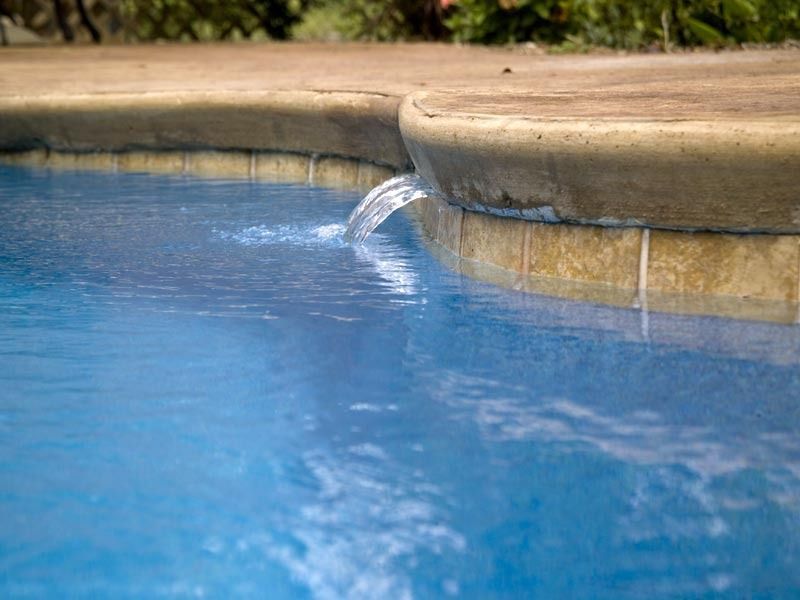 Blue pool water spilling over a stone edge into a shallow pool