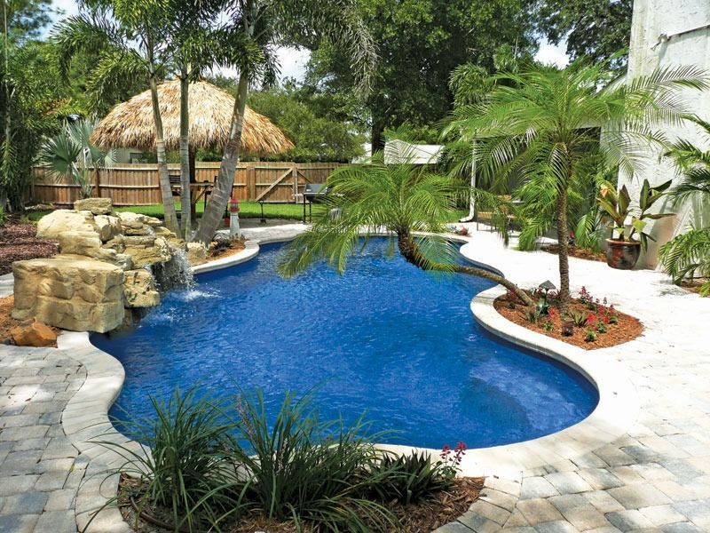 Lush tropical resort pool with blue water, rock waterfall, palm trees, and thatched cabana